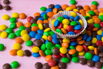 Spilled multicolored candies on a pink wooden background