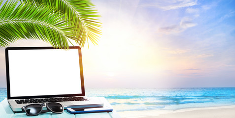 Modern laptop on blue wooden table with blank screen at tropical beach