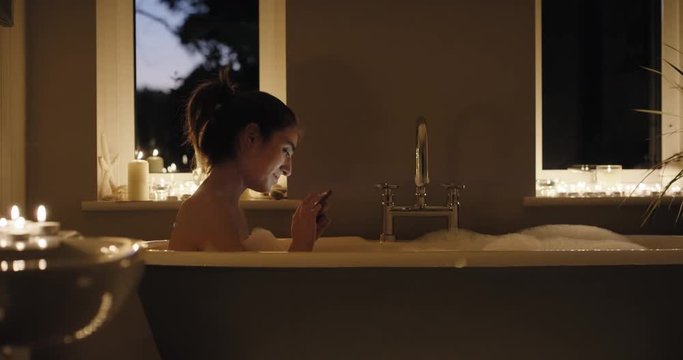 Beautiful Woman relaxing in bubble bath lying in bathtub using smartphone browsing social media sharing  photos mindfulness health concept at home