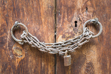 Old rusted padlock, rusted chain, and keyhole on a closed wooden aged grunge  double door