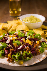 Closeup of Mexican tortillas with meat, red beans, Jalapeno pepper, nachos chips, beer and salsa guacamole