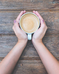 Top view image of woman's hands holding a cup of coffee on wooden vintage table