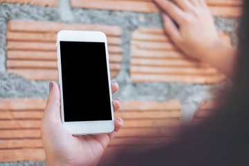 Mockup image of hand holding white mobile phone with blank black screen while lean on brick wall background