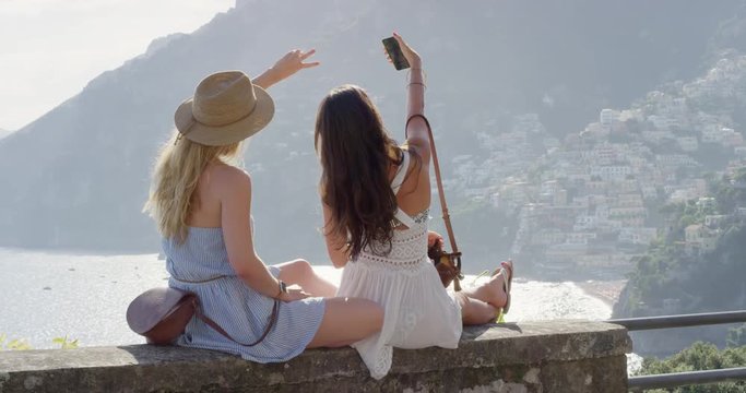 Beautiful girl friends taking selfie photograph at sunset using smartphone sharing photo on social media with mobile phone of Positano Amalfi Coast Women enjoying Italy European vacation travel adventure