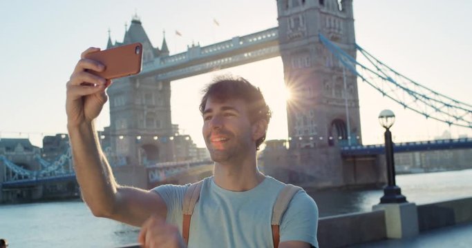 Man taking selfie photograph in city at sunrise smartphone photographing Tower bridge London enjoying Europe vacation travel adventure