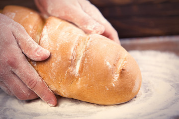 male hands holding bread loaf on the wonderful brown wooden background
