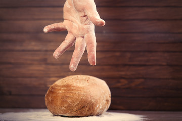 male hand under bread loaf on the wonderful brown wooden background