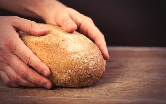 male hands holding bread loaf on the wonderful brown wooden background
