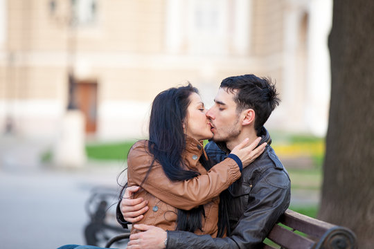 photo of cute couple sitting on the bench and kissing on the wonderful park background