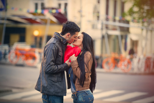 photo of cute couple holding heart shaped pillow and kissing on the wonderful street background