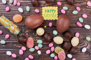 Happy Easter card, scattered sweets. Candies on dark brown wood.
