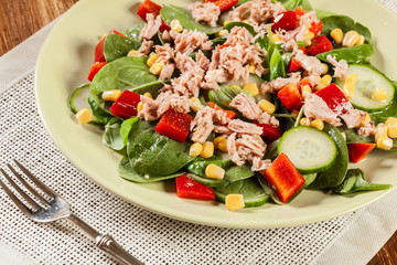 Fresh spinach salad with tuna, cucumber, corn, and red paprika on a plate