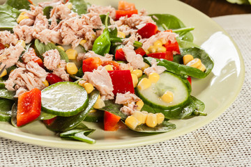 Fresh spinach salad with tuna, cucumber, corn, and red paprika on a plate