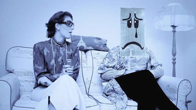 A verbose harsh wife keeps talking and watching the tv, while the husband saddens (he wears a breadbag face). Funny comedic shot. Cold color palette.
