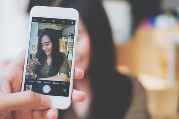 A man using white smart phone taking a picture of a beautiful woman in wooden vintage cafe