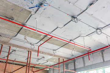 Ventilation pipes in black insulation material and fire sprinkler on red pipe are hanging from the ceiling inside new building. - obrazy, fototapety, plakaty