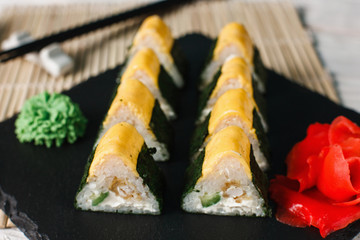 Traditional and healthy Japanese food, national cuisine. Delicious triangle sushi rolls set served on black slate with ginger and wasabi, closeup.