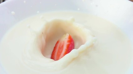 Half of strawberry falling in a white bowl with cream - Powered by Adobe