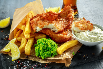 British Traditional Fish and chips with mashed peas, tartar sauce on crumpled paper with cold beer.