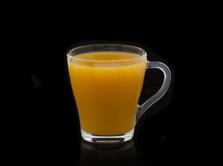 Glass with yellow juice on a black background with shadow