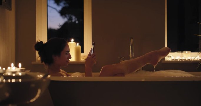 Sexy Woman lying in bubble bath taking photos of feet using smartphone sharing  on social media relaxing at home mindfulness concept