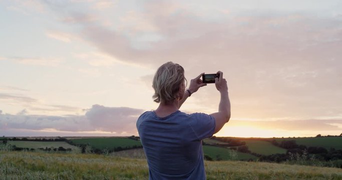 Man taking photo of wheat field using smartphone Photographing sunset nature background Rear view