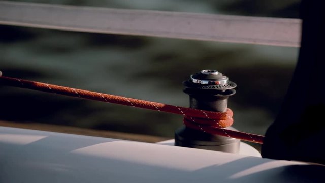 Sailor in black suit using the capstan head to fixing the rope. Close-up view of male hands twisting a cable.