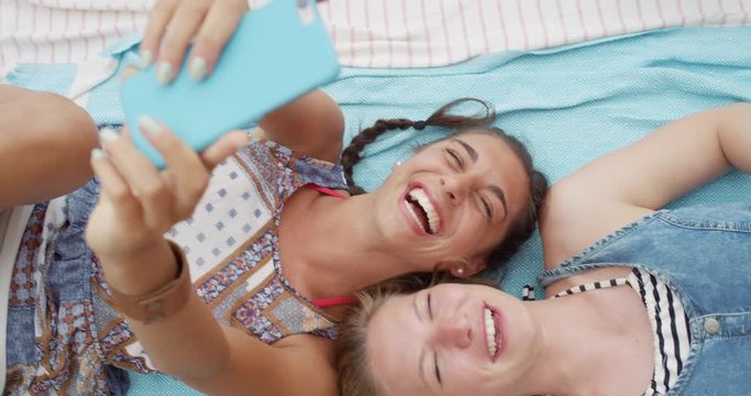Top view of teenage girl friends taking selfie photo with smart phone lying on back smiling laughing at beach direct from above