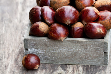 Obraz premium fresh raw chestnuts in a wooden box on wooden background