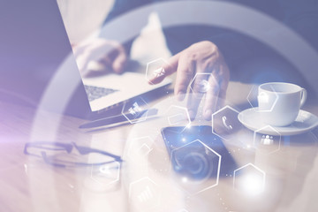 Concept of virtual screen,connections icon and digital interfaces display.Businessman working at the wooden table on laptop.Man pointing hand on thouch screen of mobile phone.Blurred background.