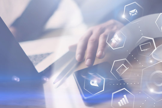 Concept of virtual screen,connections icon and digital interfaces.Closeup view of Businessman working at office on laptop.Man pointing hand on thouch screen of smartphone.Blurred background.