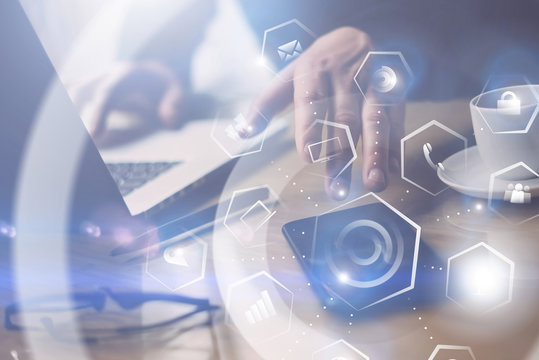 Concept of virtual screen,connections icon and digital interfaces display.Closeup view of Businessman working at the wooden table on laptop.Man pointing hand on thouch screen of mobile phone.Blurred.