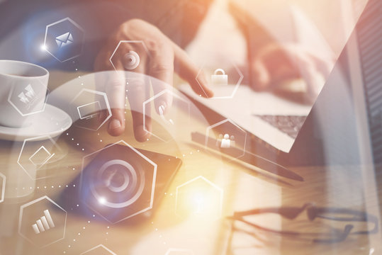 Businessman working at the wooden table on laptop.Closeup view of Man pointing hand on thouch screen of mobile phone.Concept of virtual screen,connections icon and digital interfaces display.Flares.