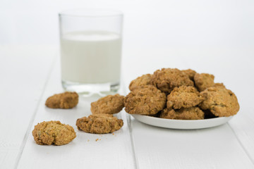 Homemade biscuits on a plate and a glass of milk on white wooden table.