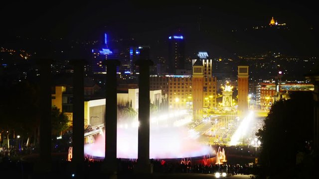 Barcelona, Spain. Famous Magic Fountain show in time-lapse at night. Motion blurred people, colorful water and Spanish square at the background in Barcelona, Spain. Dark clear sky, car trails