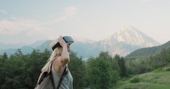 Young woman hiker exploring wilderness mountains wearing virtual reality headset in nature watching 360 travel video imagination concept enjoying summer trekking in Italian Alps