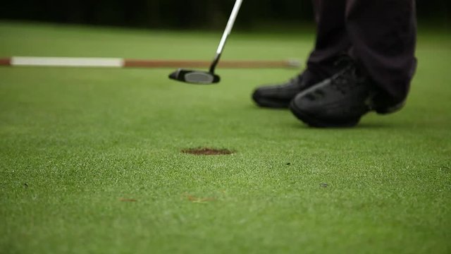 legs feet male professional golfer using putter to hole the ball (close up).