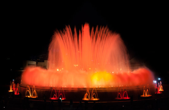 Throngs of people at colourful light & water fountain show.  Night at Magic Fountain in Barcelona.  Large attraction turns on at night & provides entertainment for all ages on a warm evening.