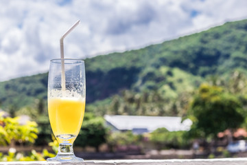 Glass of orange juice on bright tropical blurred background with palms, outdoors. Tropical Bali island, Indonesia.