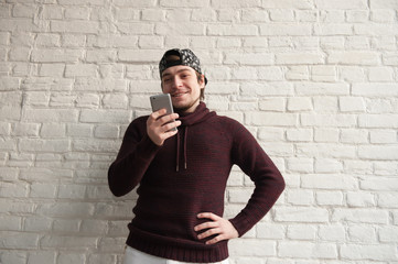 Obraz premium smiling young man wearing cap looking into smartphone in his hand