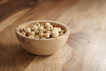 roasted hazelnuts in wood bowl on wooden table, copy space on the right side
