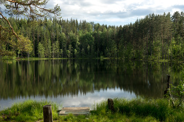 Fototapeta na wymiar Beautiful lake with reflection of blue sky and evergreen forest in the north of Russia 