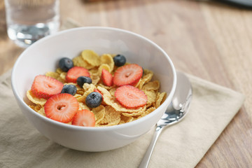 dry corn flakes with berries in bowl on table, breakfast preparation