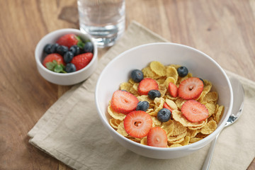 dry corn flakes with berries in bowl on table, breakfast preparation