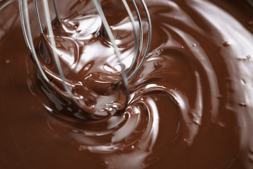 closeup of steel whisk in melted dark premium chocolate, shallow focus