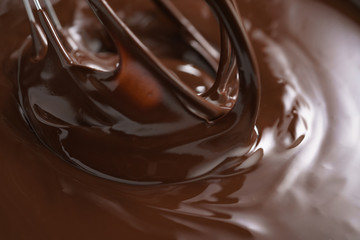 closeup of steel whisk in melted dark premium chocolate, shallow focus