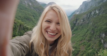 Beautiful woman taking selfie video using smartphone outdoors Girl sharing photograph on social media with mobile phone enjoying Norway  vacation travel adventure