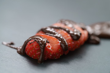 sliced ripe strawberry with dark premium chocolate on slate board, shallow focus