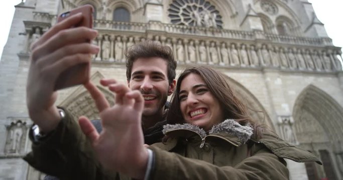 Tourist couple taking selfie photograph in front of Notre Dame Paris smartphone in city sharing lifestyle photo enjoying  holiday European   vacation travel adventure 