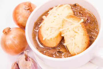 Onion soup with toast on a white background with some onions and garlic